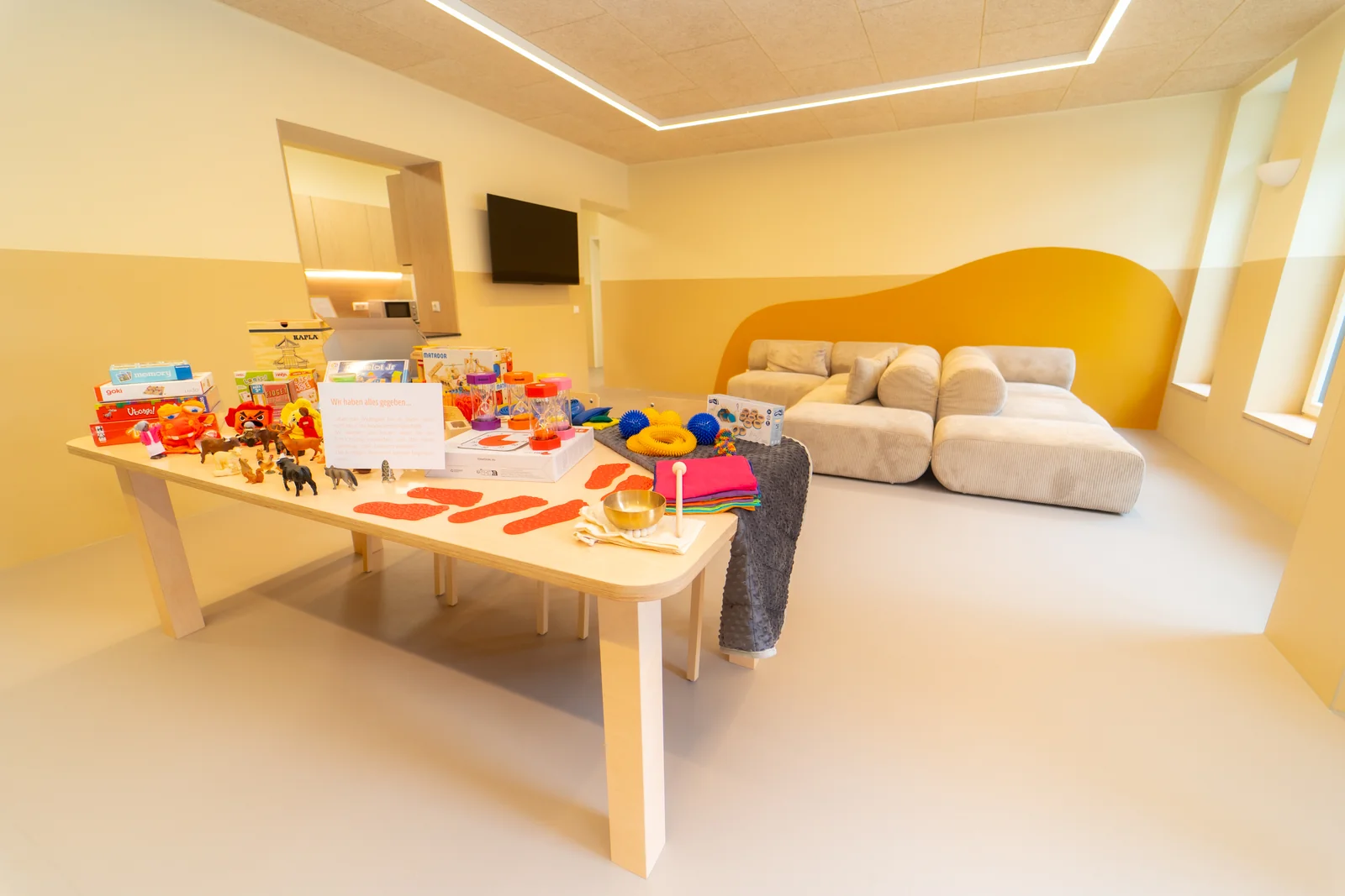 Heller Gemeinschaftsraum im Walter-Purschke-Haus mit großem Tisch, Spielmaterial und Sofabereich