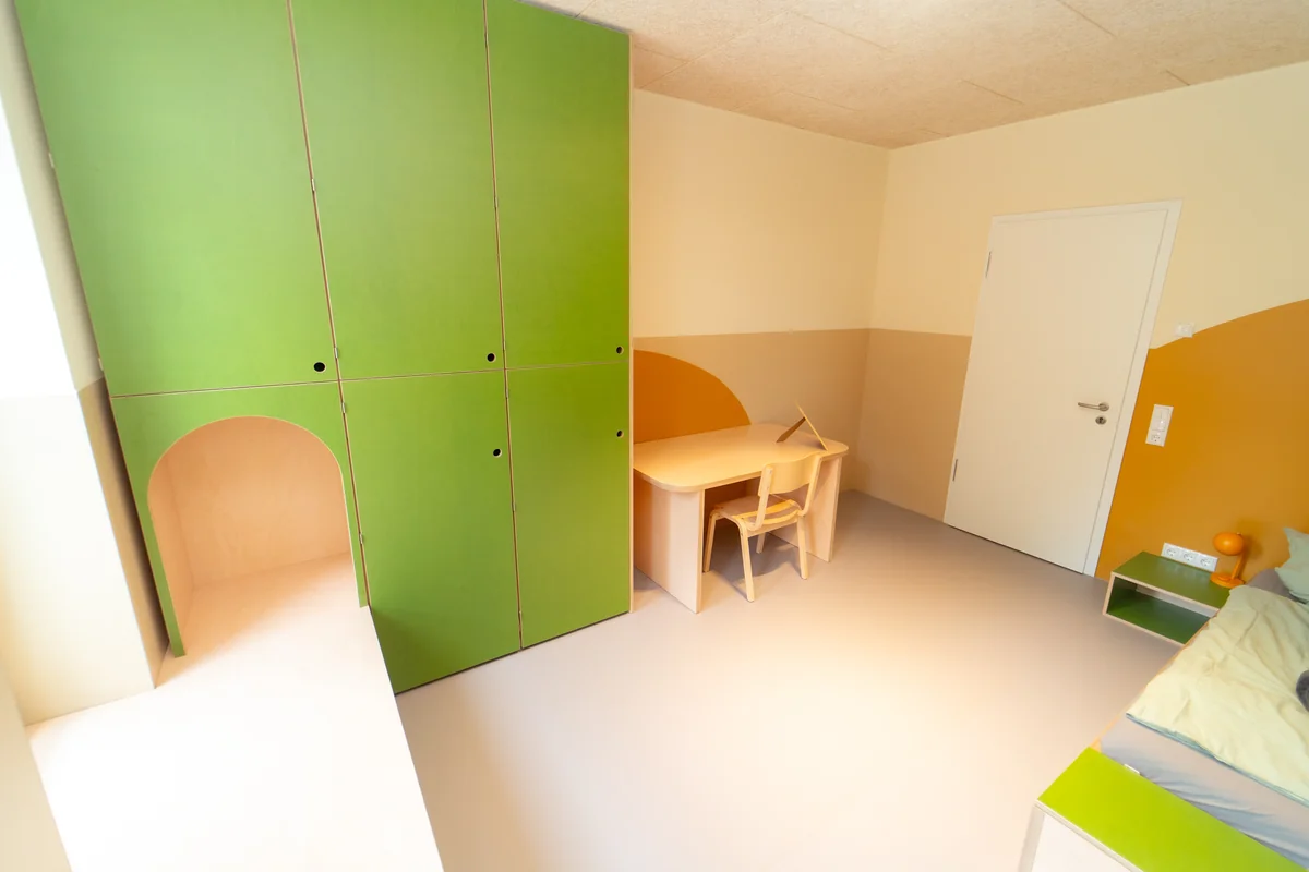Kinderzimmer mit grünem Einbauschrank, kleinem Schreibtisch und eigenem Schlafbereich